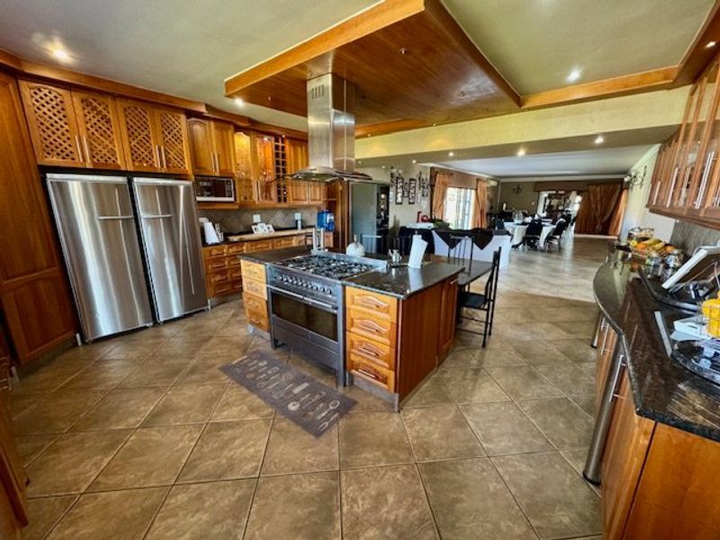 Spacious open-plan kitchen featuring extensive wooden cabinetry, granite countertops, a central gas range with extractor, and tiled flooring, flowing into the living and dining areas.