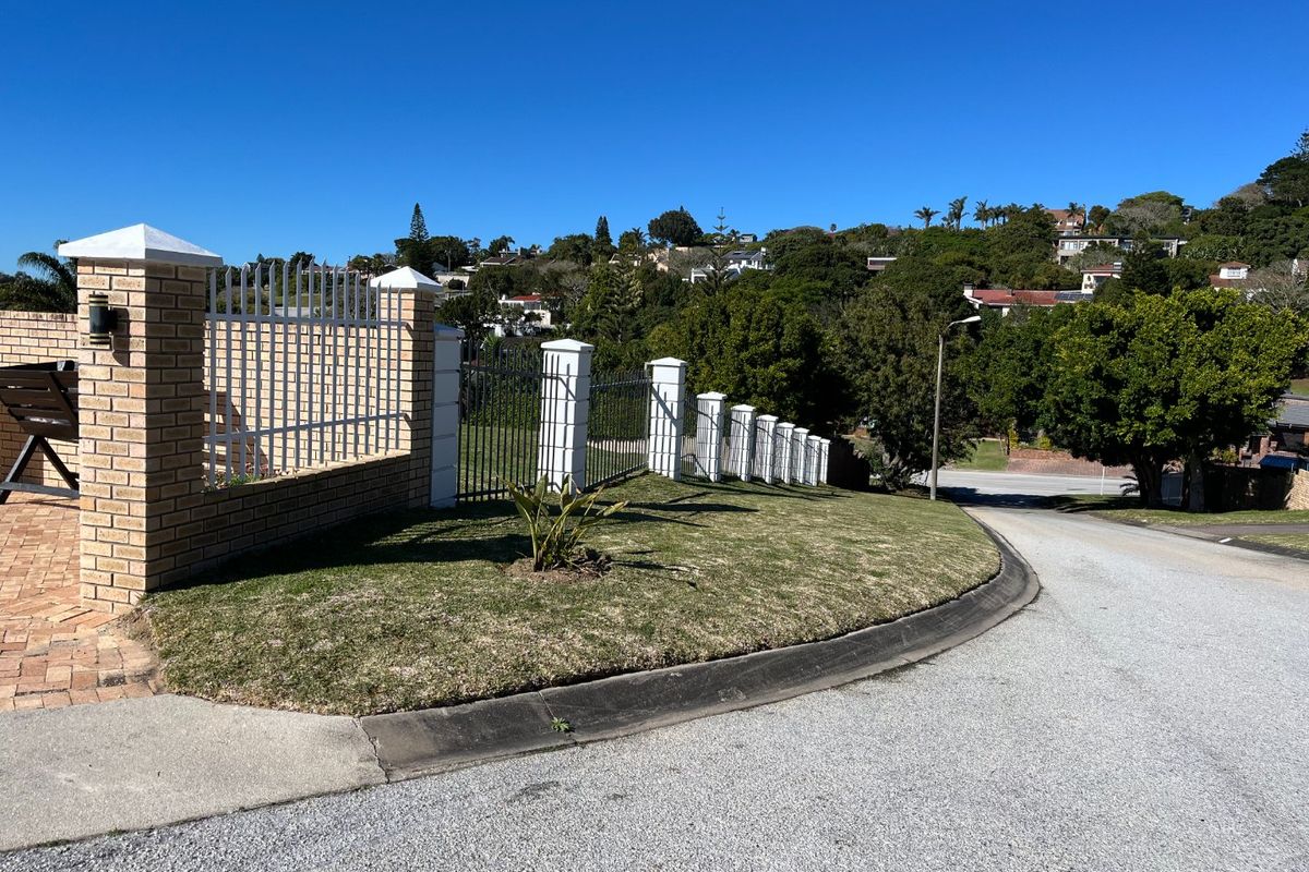 A street-level view of the property boundary featuring a brick and metal security fence, manicured lawn, and asphalt road frontage.