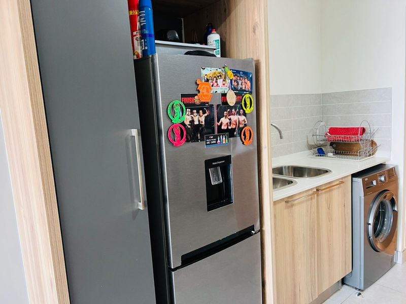A compact kitchen area featuring modern wood-look cabinetry, a stainless steel sink with mixer tap, tiled splashback, and a built-in washing machine.