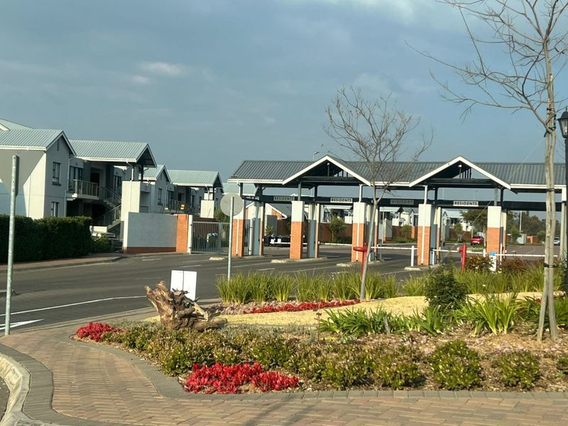 View of the apartment complex entrance featuring a secure gatehouse, paved access lanes, and well-maintained landscaped garden areas.
