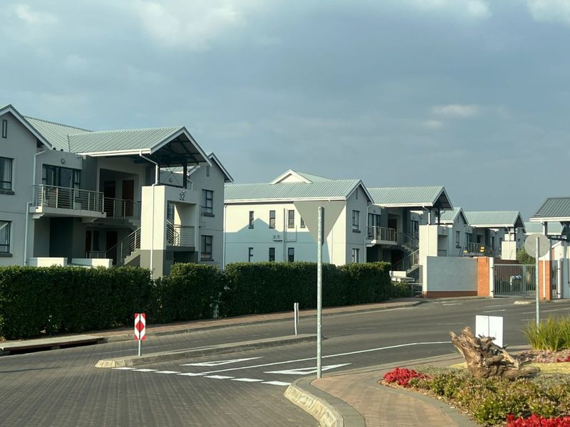 A street-level view of a modern apartment complex featuring multiple residential buildings with metal roofs, balconies, and well-maintained landscaped grounds.