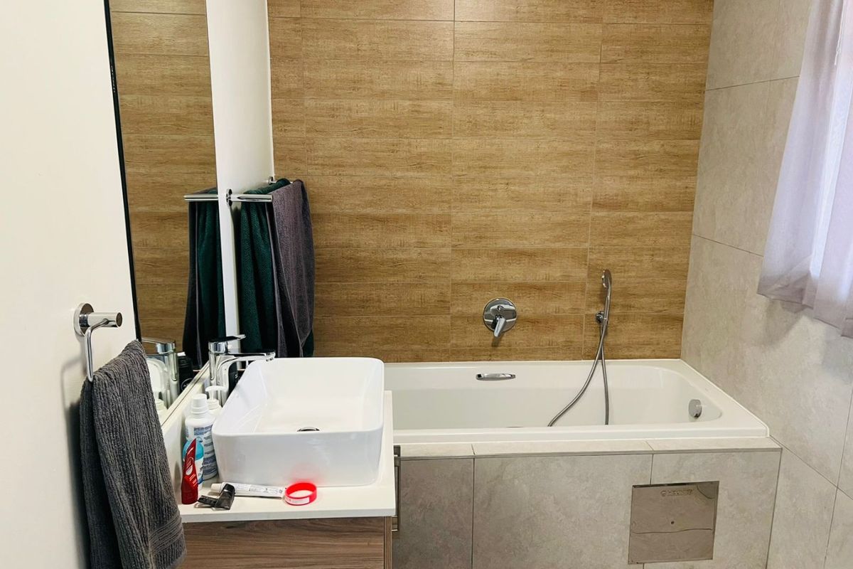 Modern bathroom featuring a built-in bathtub with handheld shower, a vessel sink vanity, and contemporary wood-look and neutral wall tiling.