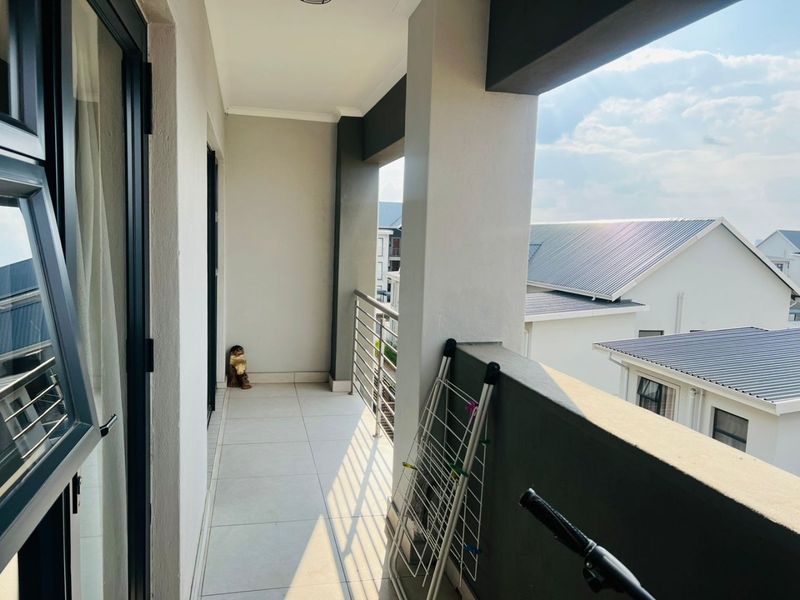 A covered balcony featuring tiled flooring, metal balustrades, and access via a sliding door, offering an open outdoor space.