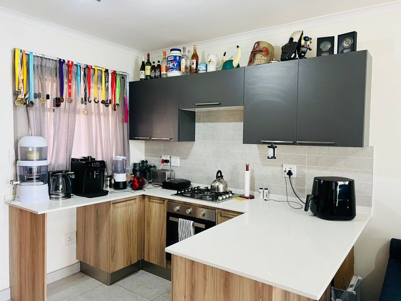 Modern kitchen featuring wood-finish cabinetry, stone countertops, a gas hob, built-in oven, and a tiled backsplash.