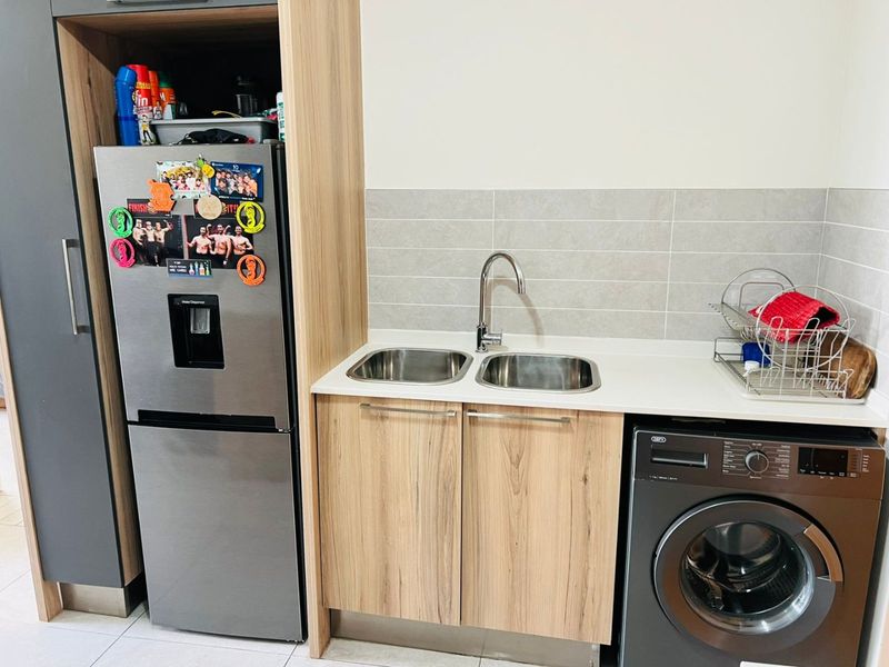 A modern, compact laundry area featuring light wood-grain cabinetry, a double stainless steel sink, and integrated space for a washing machine.