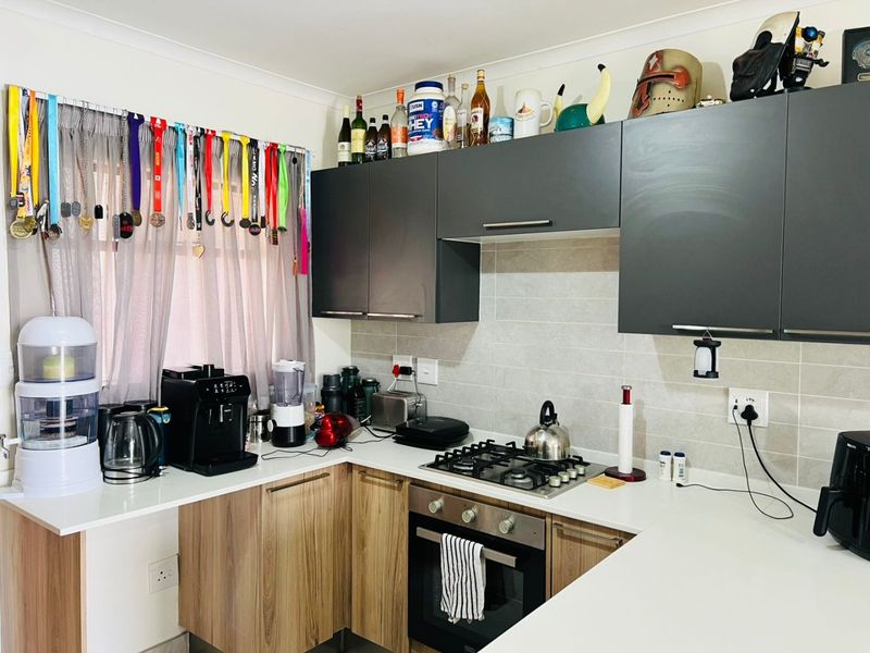 A functional kitchen featuring modern laminate cabinetry, stone countertops, a gas hob, and a built-in oven with a neutral tiled backsplash.