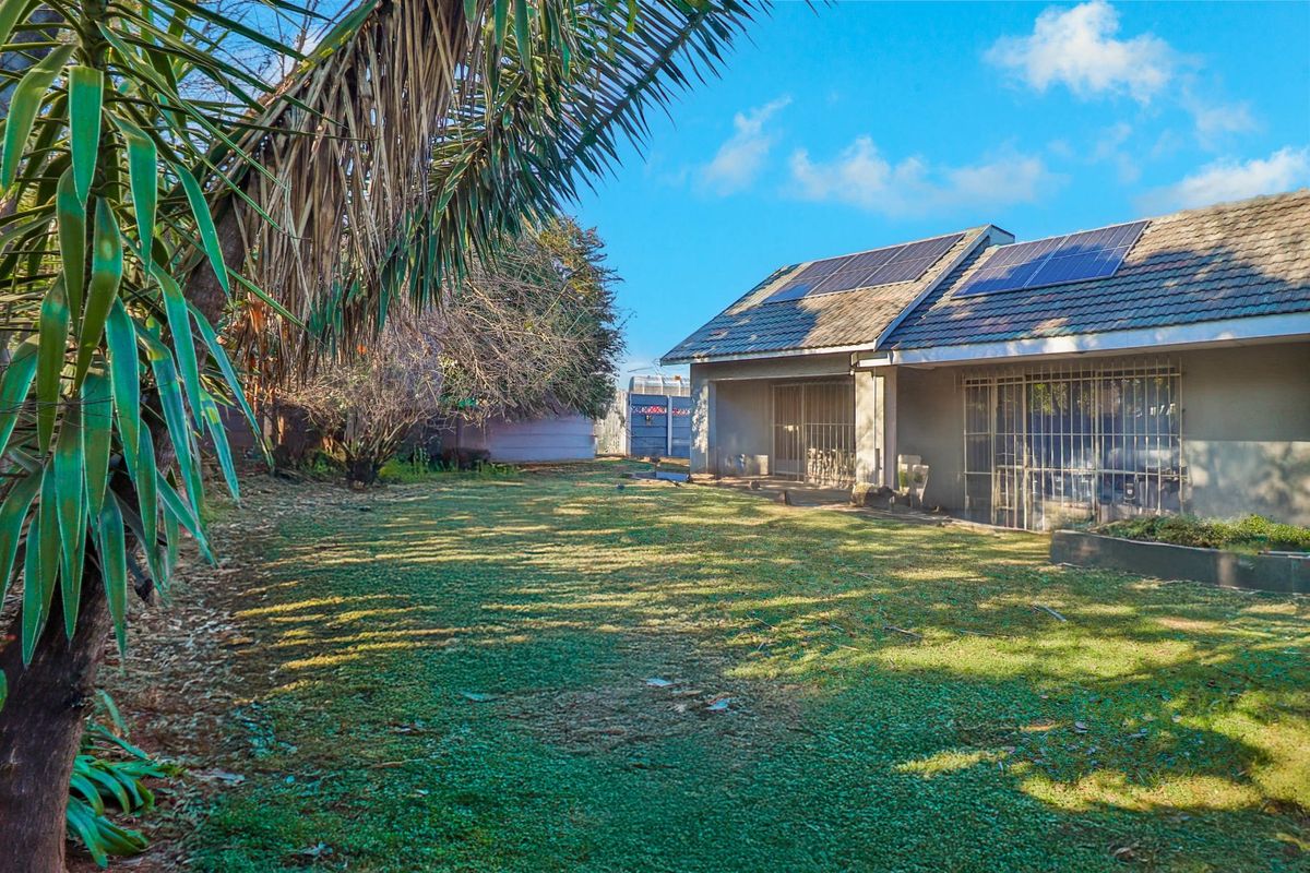 Rear view of the property featuring a spacious lawn, tiled roof with installed solar panels, and secure access points.