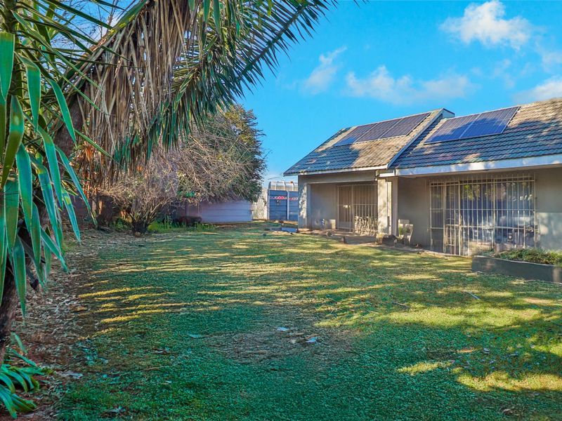 Rear view of the property featuring a spacious lawn, tiled roof with installed solar panels, and secure access points.
