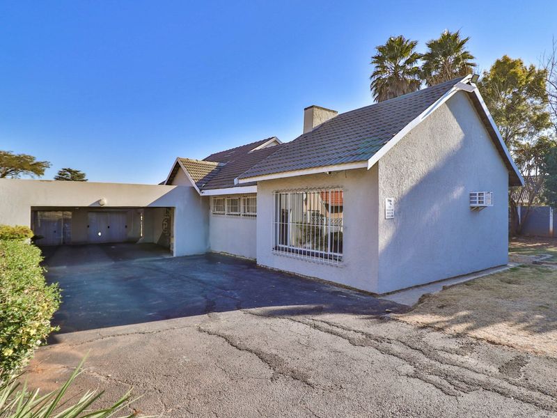 Front view of a single-story house featuring a tiled roof, a covered carport, and a paved driveway with visible surface cracking.