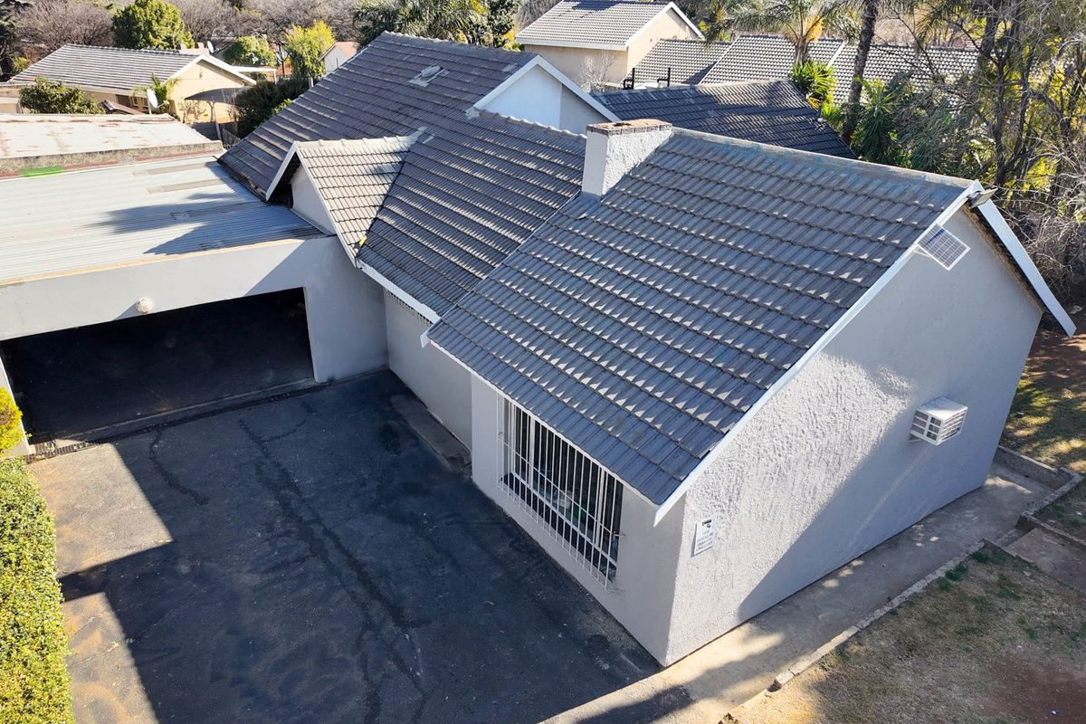 Aerial view of the property showing the tiled roof, carport, driveway, and exterior facade with security bars.