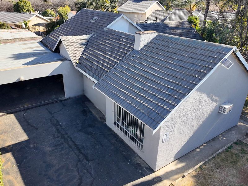 Aerial view of the property showing the tiled roof, carport, driveway, and exterior facade with security bars.