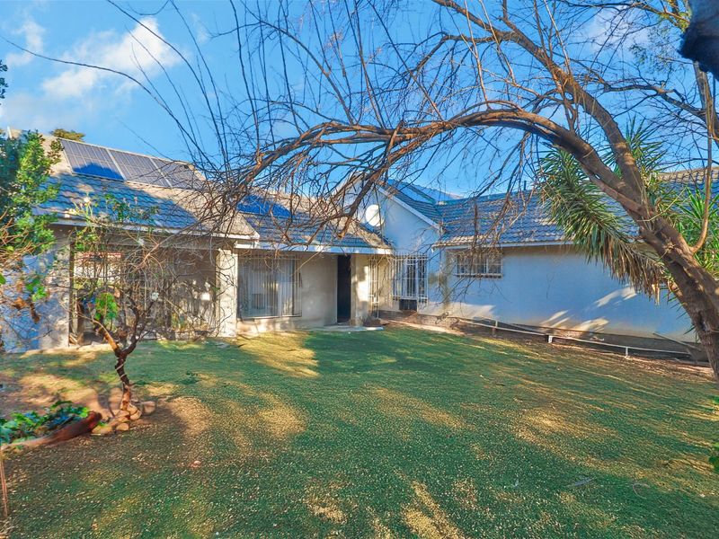 Rear view of the house featuring a tiled roof with installed solar panels, security bars on windows, and a private garden area.
