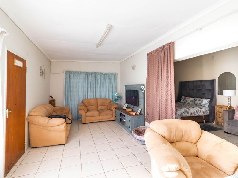 Open-plan living area featuring tiled flooring and a neutral color palette, with an adjoining bedroom space separated by a curtain.