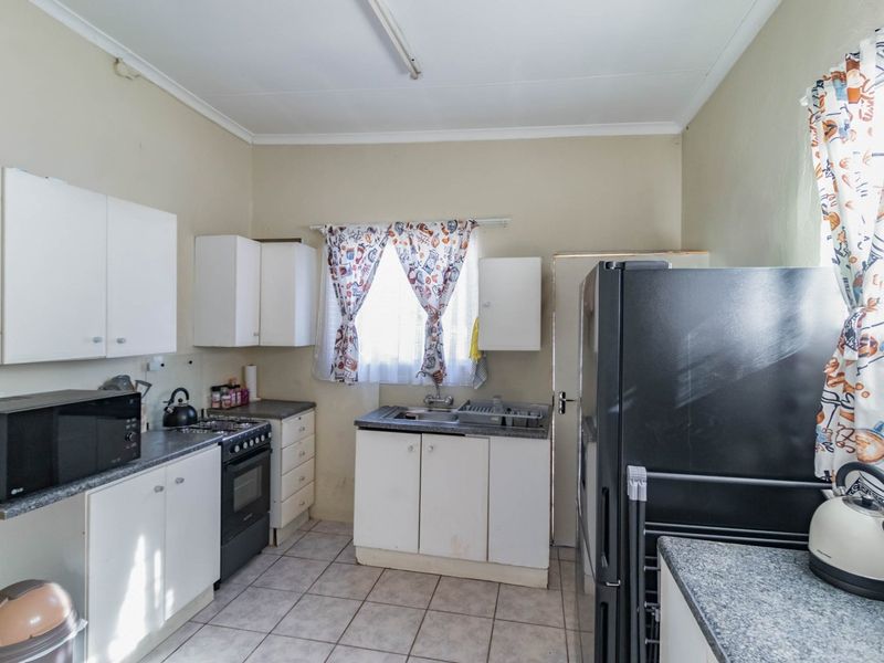A functional kitchen featuring white cabinetry, laminate countertops, tiled flooring, and a freestanding stove, offering a practical layout for daily meal preparation.