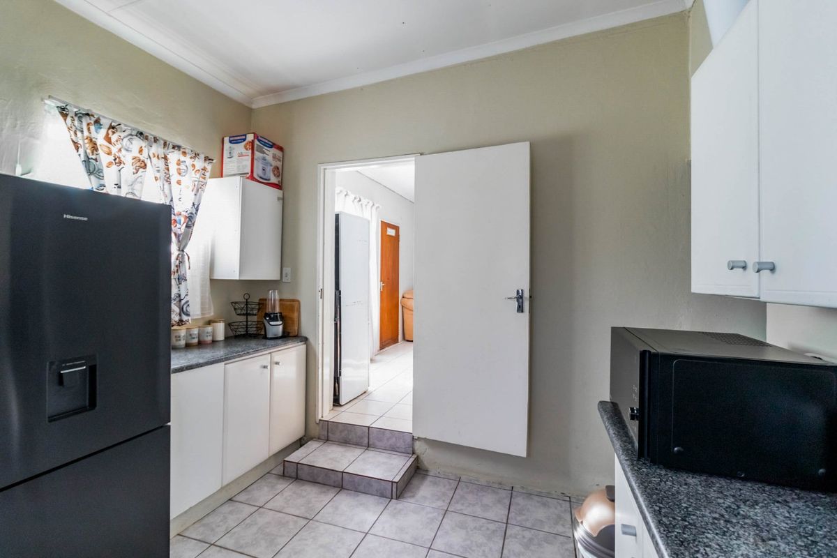 A functional kitchen featuring white cabinetry, dark laminate countertops, and tiled flooring with a step-up transition to the adjacent room.
