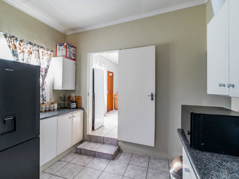 A functional kitchen featuring white cabinetry, dark laminate countertops, and tiled flooring with a step-up transition to the adjacent room.