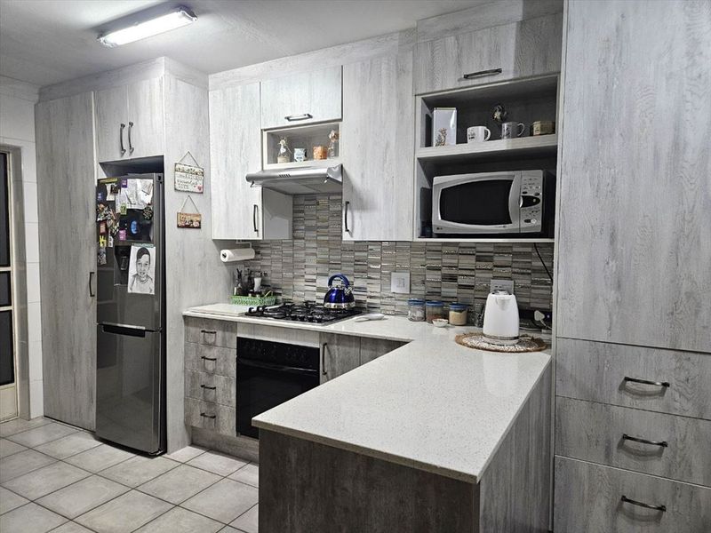 Modern kitchen featuring light wood-grain cabinetry, stone countertops, a gas hob, built-in oven, and a decorative tiled backsplash.