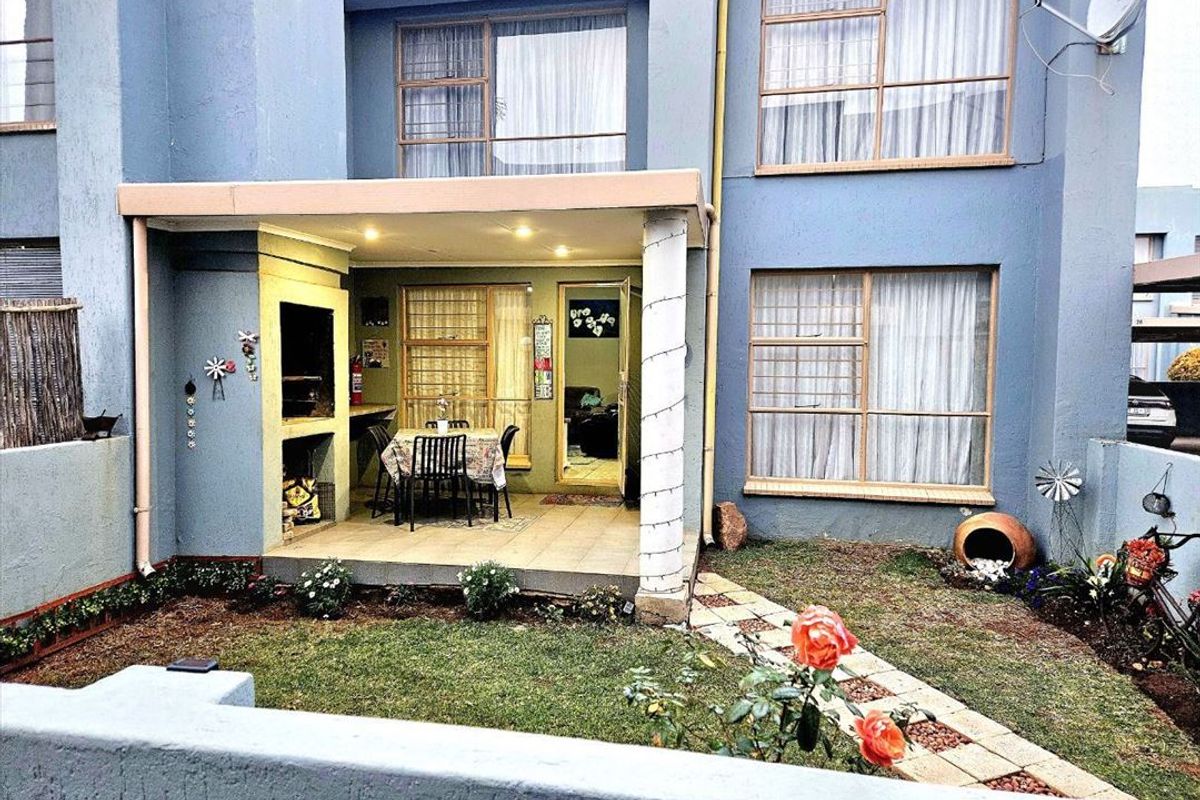 Rear view of the townhouse featuring a covered patio with a built-in braai, tiled flooring, and a small private garden area.