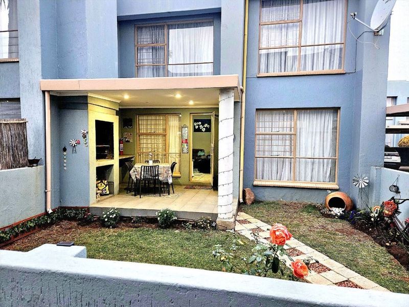 Rear view of the townhouse featuring a covered patio with a built-in braai, tiled flooring, and a small private garden area.