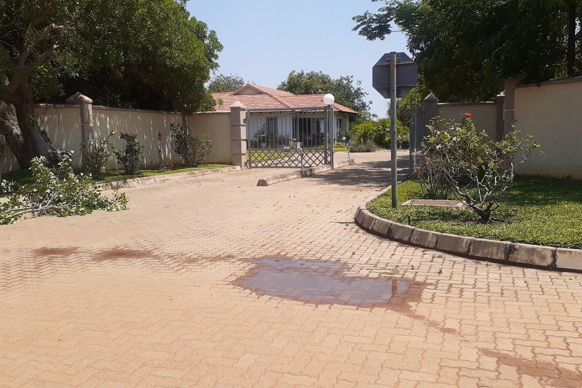 Front entrance view of the residential property featuring a paved driveway, perimeter walling, and gated access.