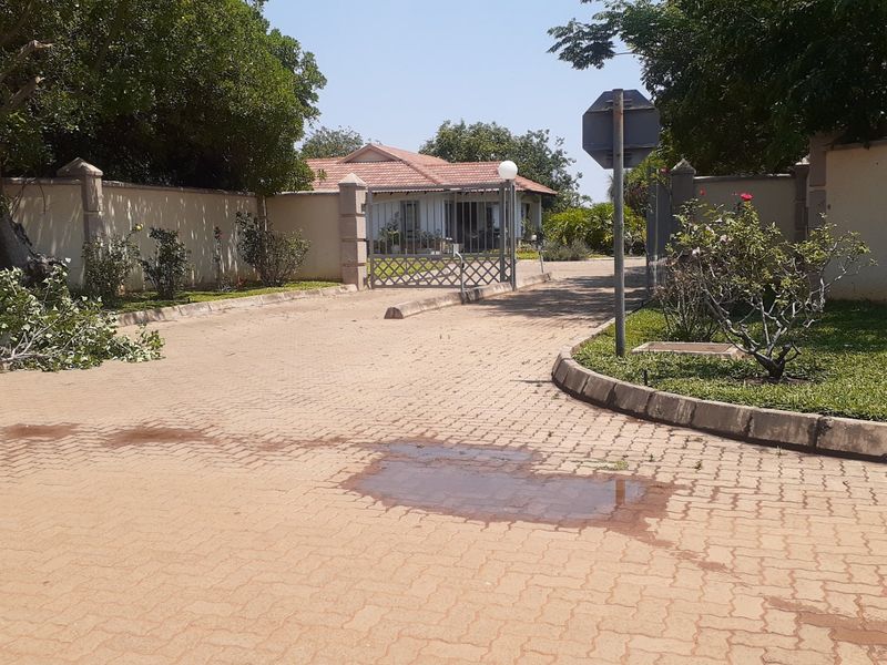 Front entrance view of the residential property featuring a paved driveway, perimeter walling, and gated access.