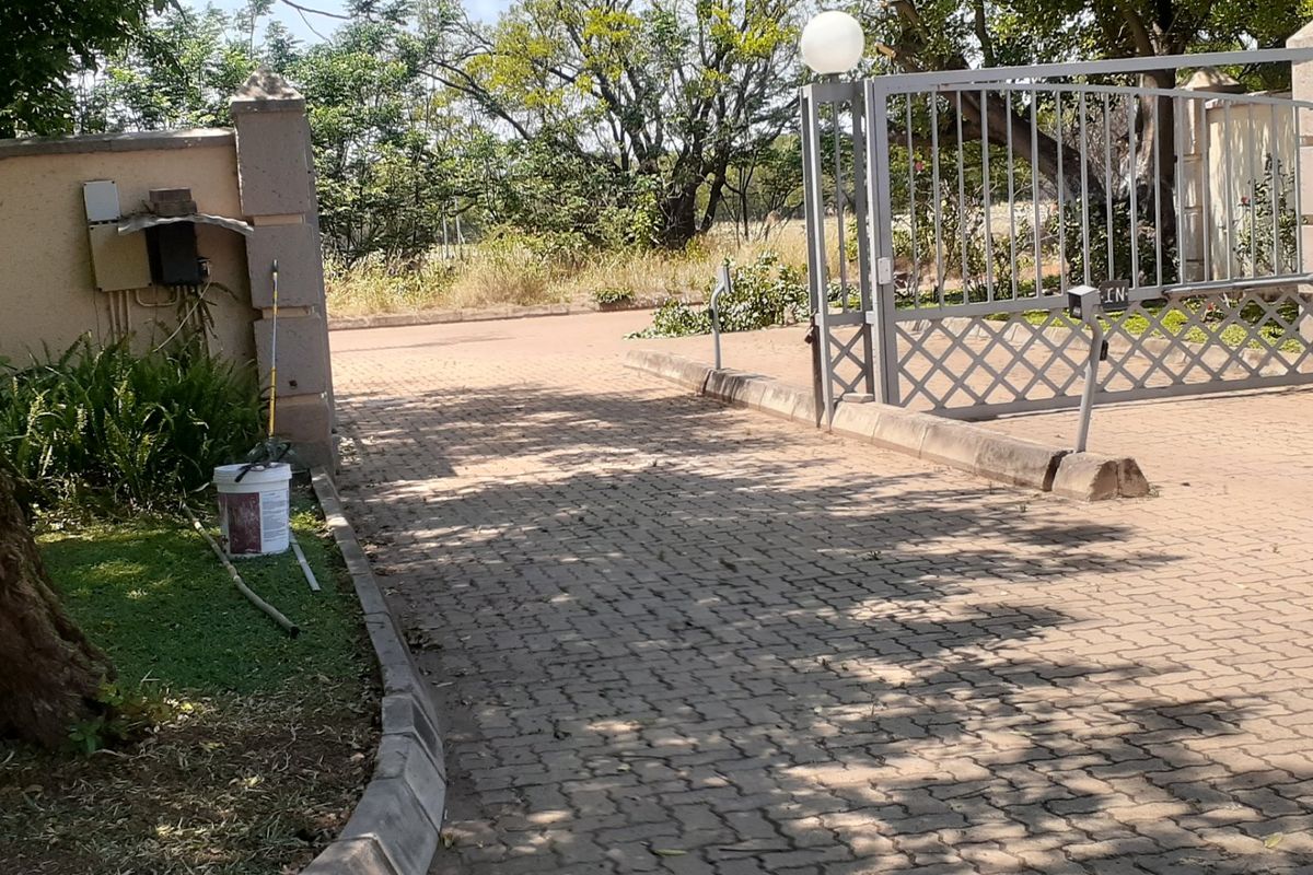 Front entrance view of the property featuring a paved driveway, metal security gate, and concrete pillars.
