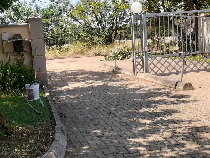 Front entrance view of the property featuring a paved driveway, metal security gate, and concrete pillars.