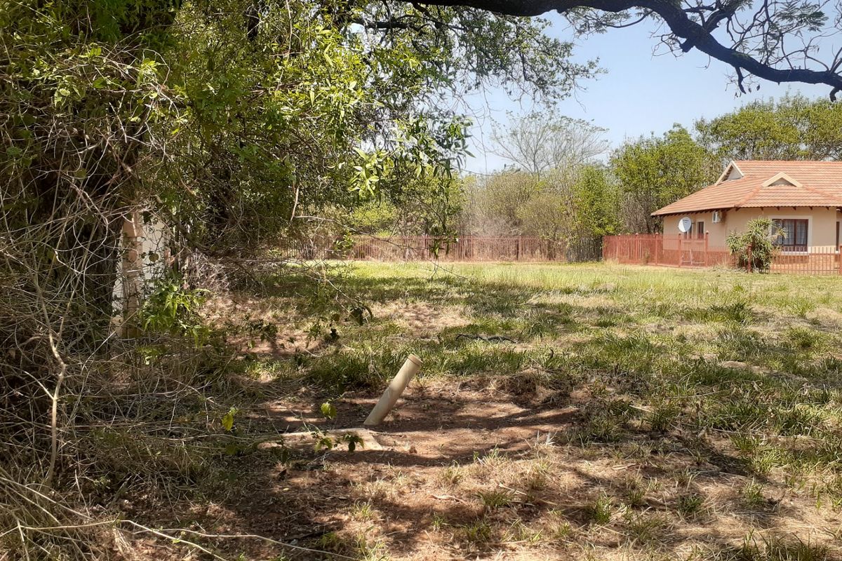 A view of the residential vacant land featuring mature trees, natural grass coverage, and perimeter fencing with an adjacent dwelling visible.