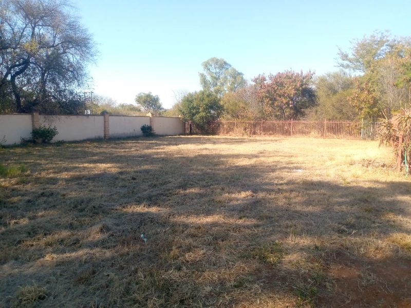 A vacant residential plot featuring a level grass area enclosed by a perimeter wall and metal fencing.