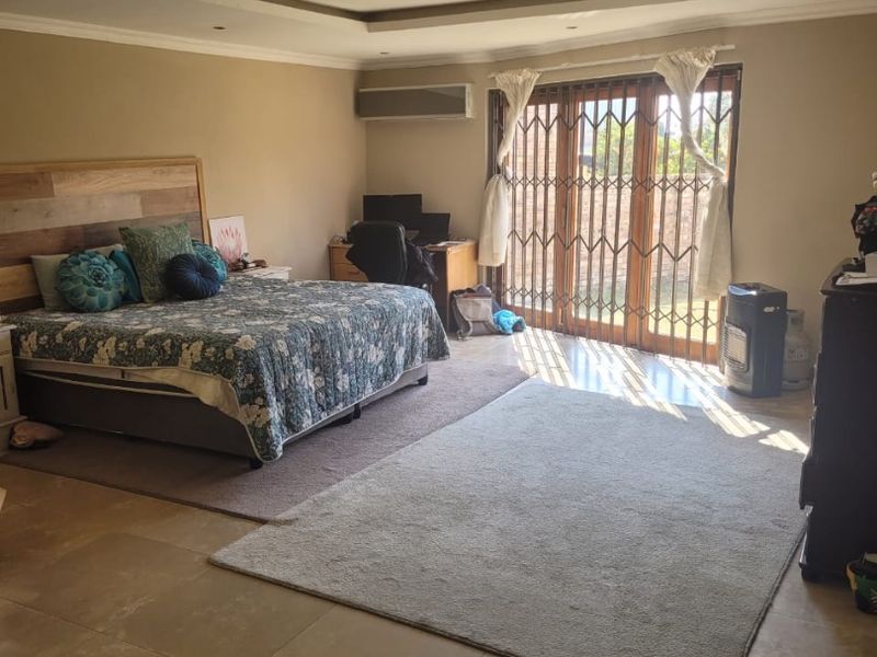 Spacious bedroom featuring tiled flooring, a recessed ceiling with downlights, air conditioning, and sliding glass doors with security gates leading outdoors.