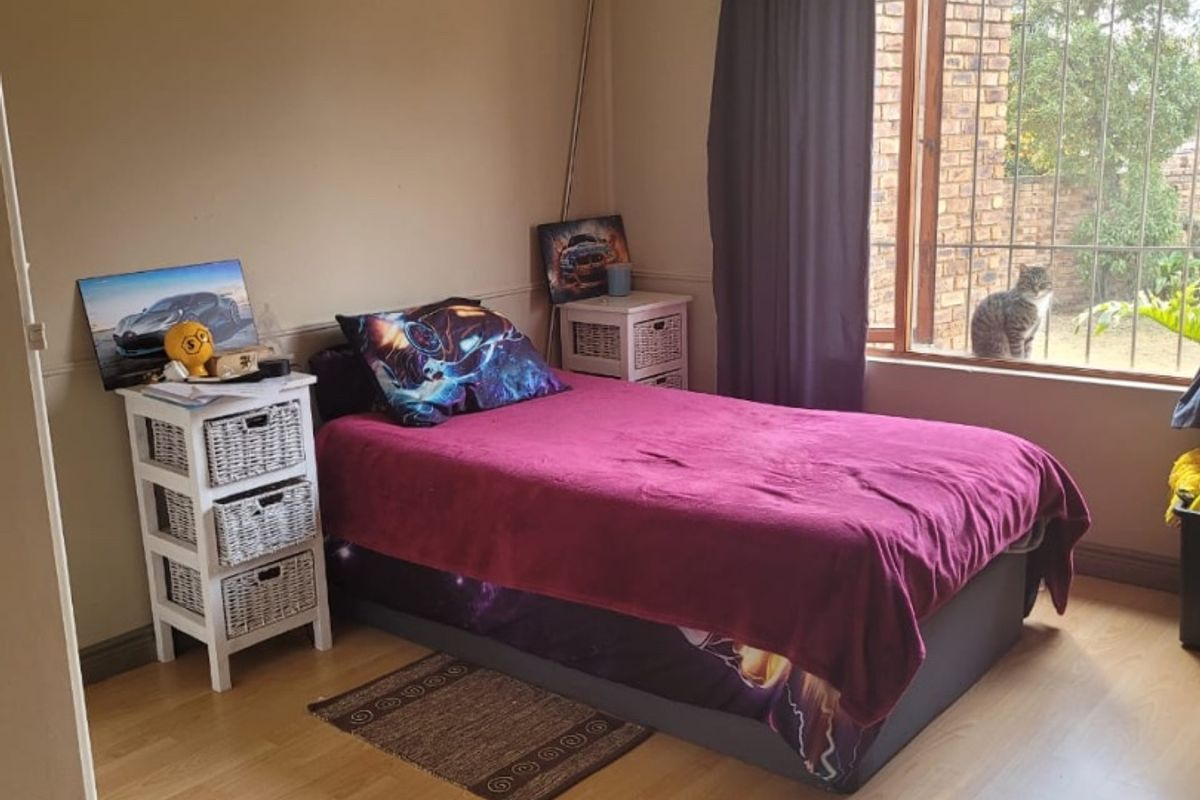 A bedroom featuring laminate flooring, recessed downlights, and a window fitted with security bars.