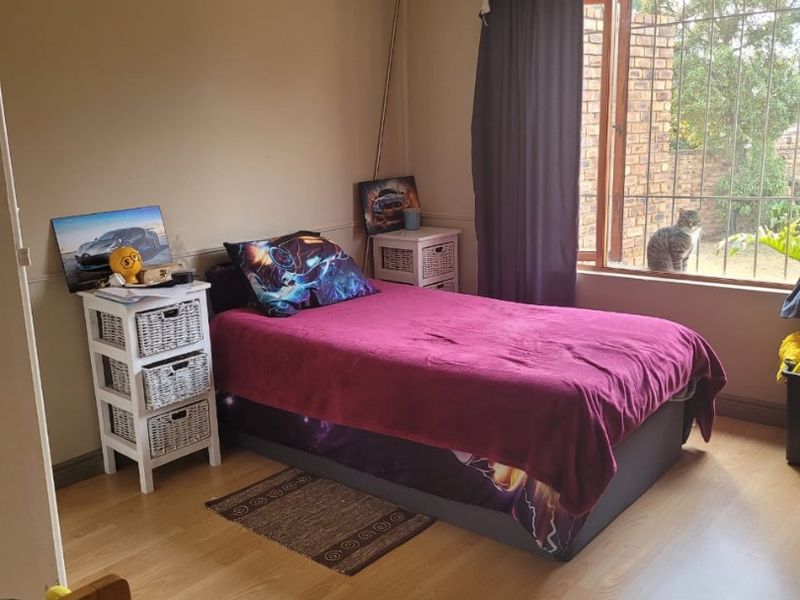 A bedroom featuring laminate flooring, recessed downlights, and a window fitted with security bars.