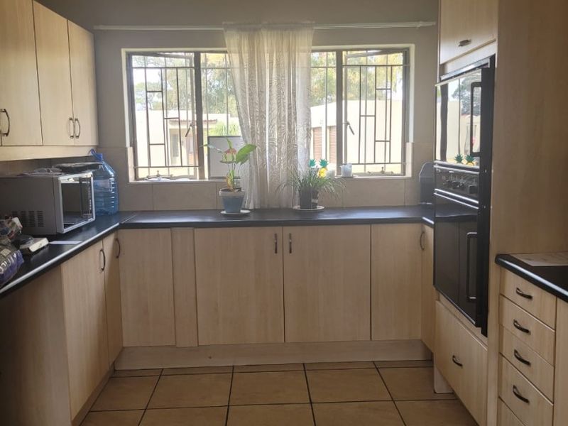 A functional kitchen featuring light wood-tone cabinetry, dark laminate countertops, built-in oven, and tiled flooring with security-barred windows.