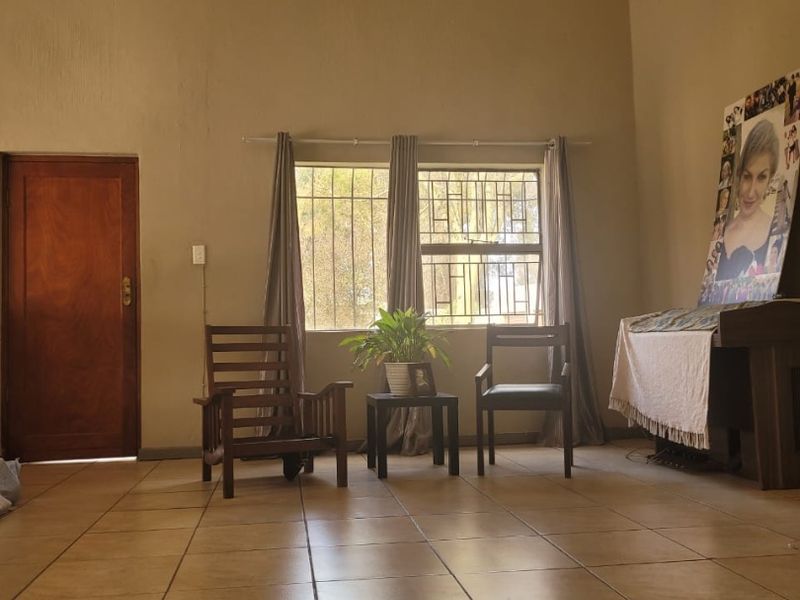 Spacious living area featuring vaulted ceilings with exposed rafters, ceramic tiled flooring, and natural light through windows fitted with security bars.