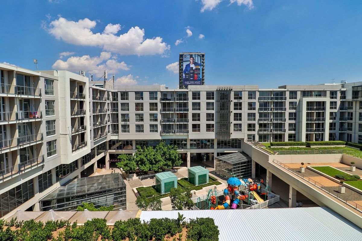 Elevated view of an apartment complex courtyard featuring landscaped gardens, a children's playground, and modern building facades with private balconies.