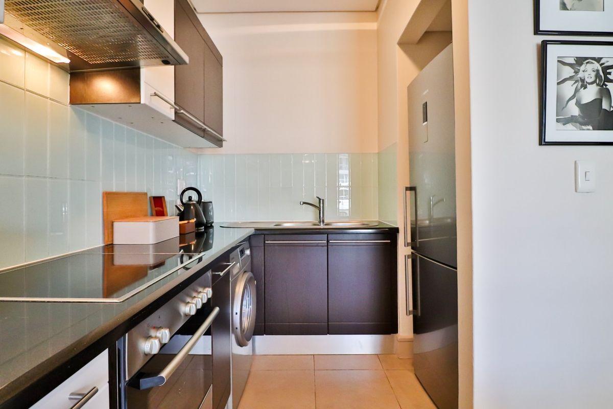 Compact modern kitchen featuring dark cabinetry, stainless steel appliances, integrated oven and hob, and a clean tiled backsplash.