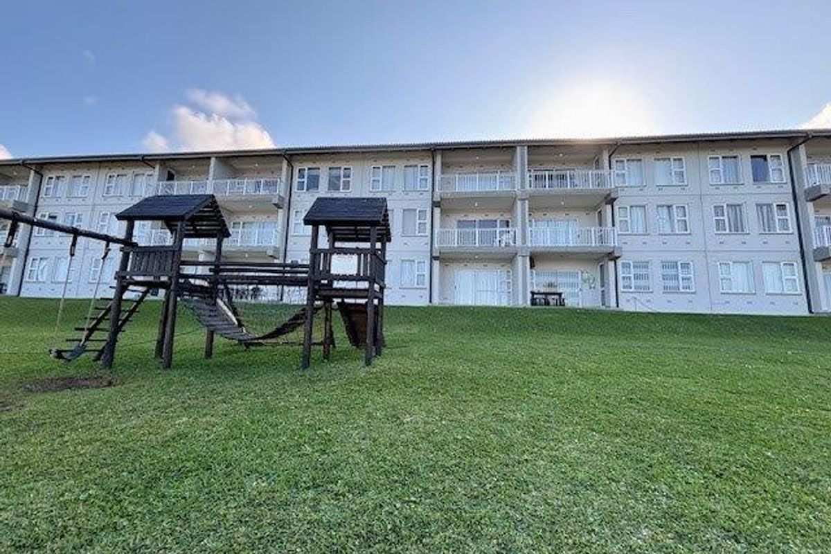 Rear view of a multi-story apartment complex featuring private balconies and a large communal grass area.