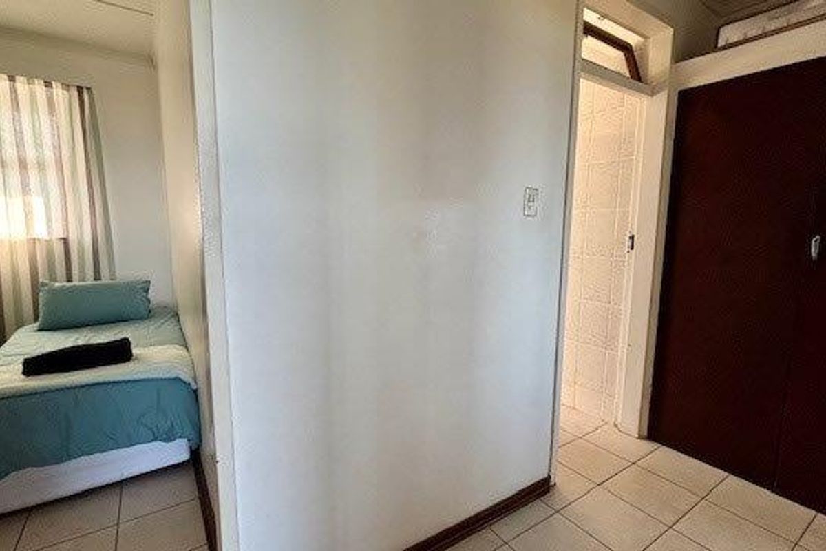 A bedroom featuring tiled flooring and built-in cupboards, with an adjacent doorway leading to an en-suite bathroom.
