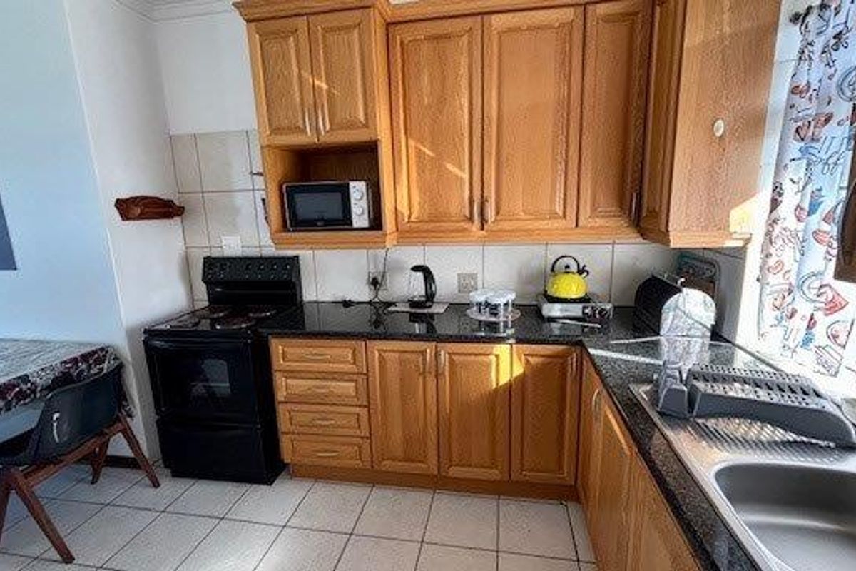 A functional kitchen featuring wooden cabinetry, granite countertops, a stainless steel sink, and an electric stove with tiled flooring and backsplash.