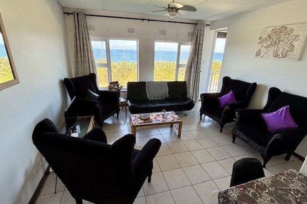 A bright living room featuring tiled flooring, a ceiling fan, and large windows offering scenic ocean views.