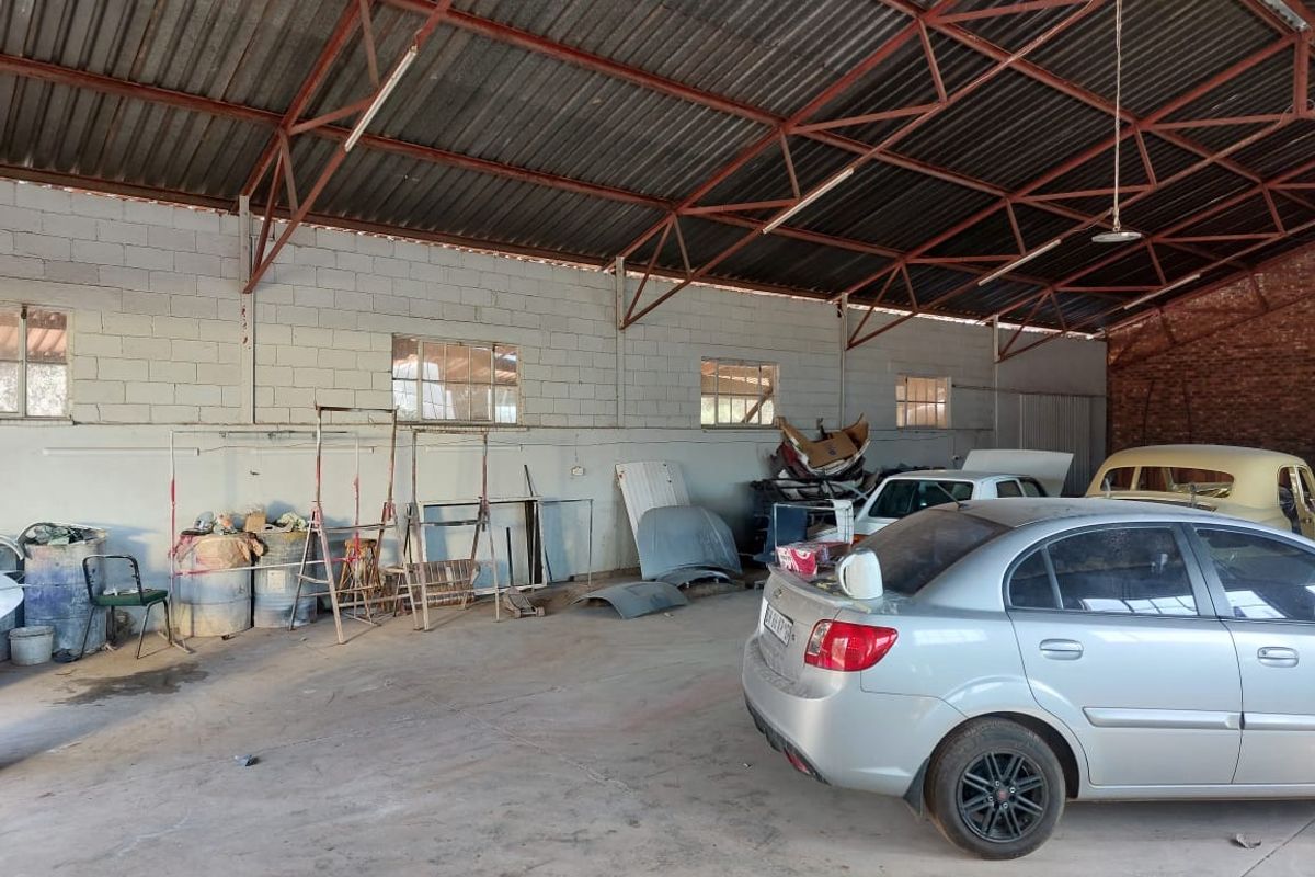 Spacious industrial garage featuring exposed steel roof trusses, concrete block walls, and durable concrete flooring, suitable for workshop or storage use.