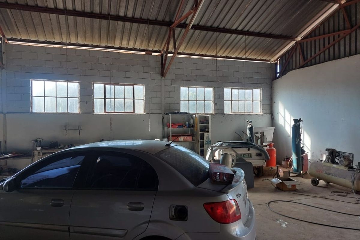 Spacious industrial garage featuring exposed steel roof trusses, concrete block walls, and large steel-framed windows, providing ample natural light and functional workspace.