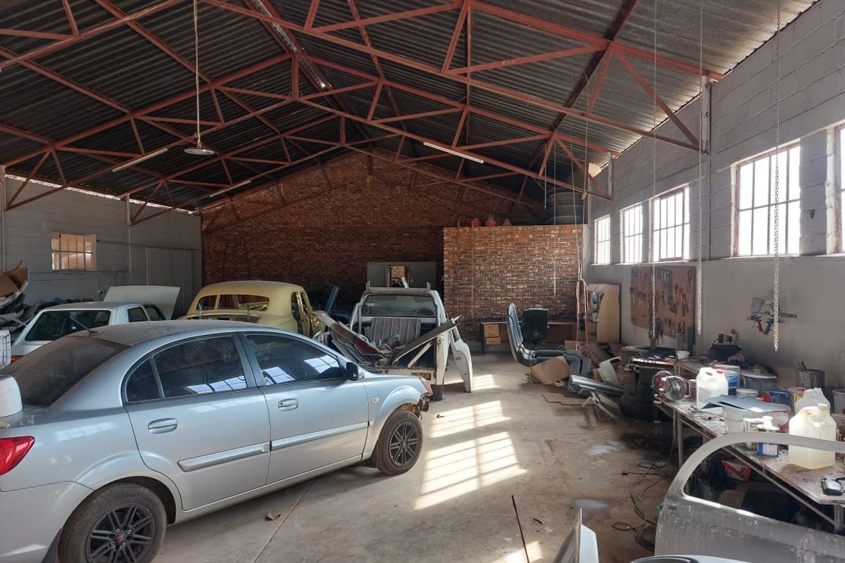 Spacious industrial garage featuring exposed steel roof trusses, concrete flooring, and brick wall finishes, suitable for workshop or storage use.