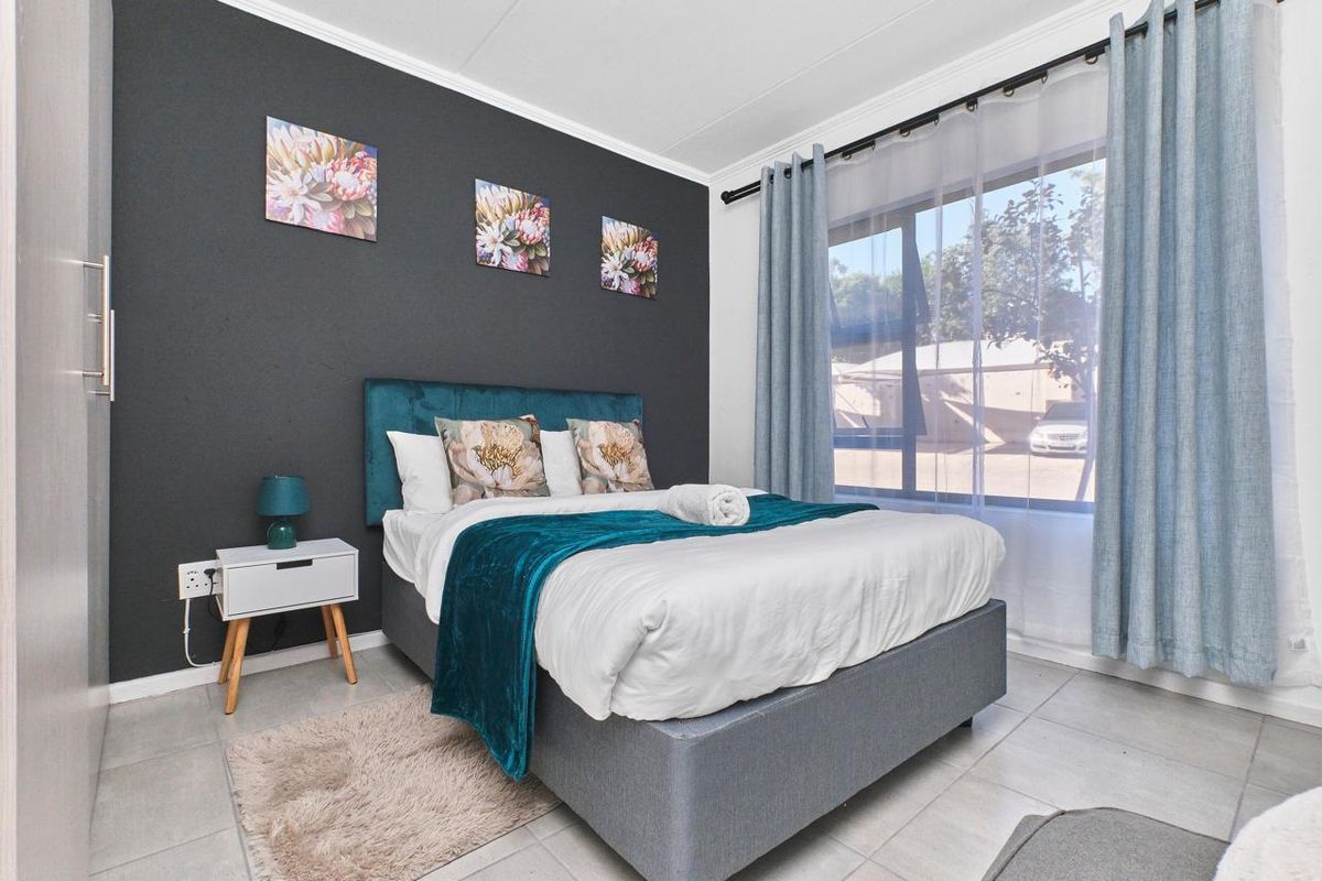 A well-maintained bedroom featuring a dark accent wall, tiled flooring, and a large window allowing for ample natural light.