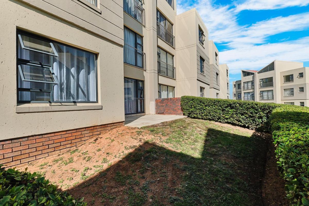 Rear exterior view of the townhouse complex featuring a paved patio area, metal balcony railings, and a small private garden space.
