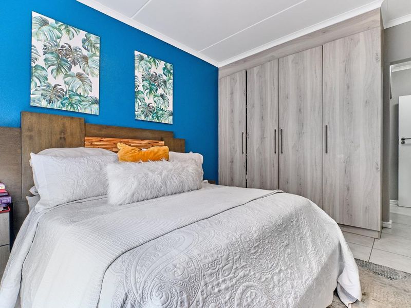 A well-maintained bedroom featuring modern light wood-grain built-in cupboards, tiled flooring, and a vibrant blue accent wall.