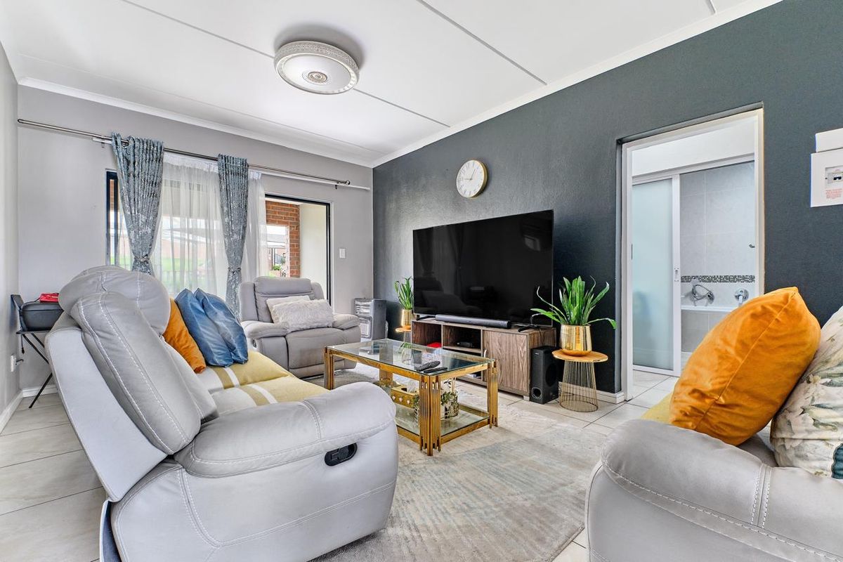 A well-maintained living room featuring tiled flooring, a dark accent wall, and direct access to an outdoor area via a sliding door.