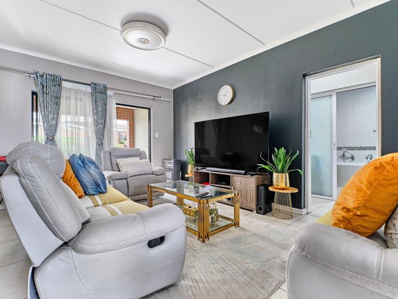 A well-maintained living room featuring tiled flooring, a dark accent wall, and direct access to an outdoor area via a sliding door.
