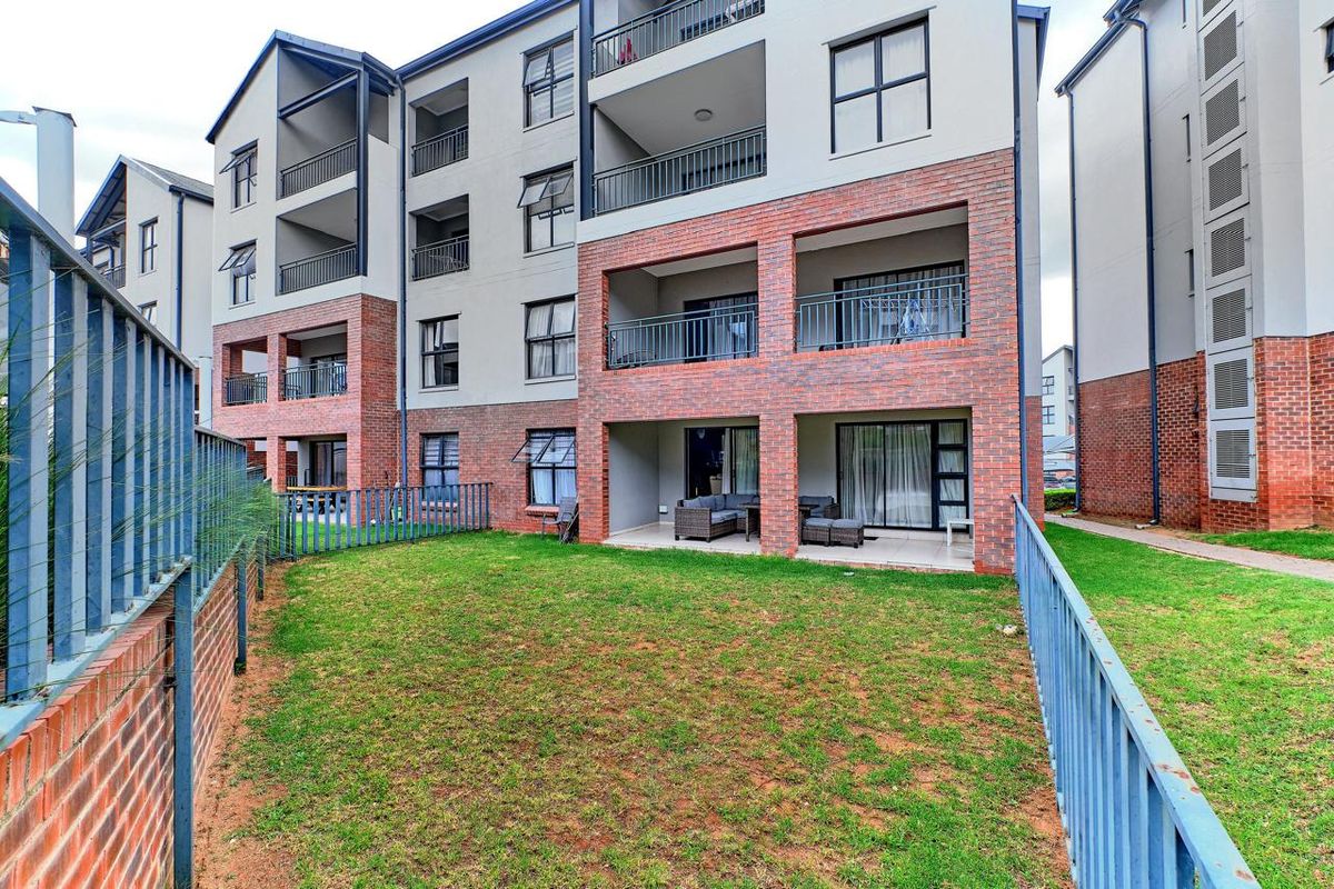 Rear view of a multi-story townhouse complex featuring brick and plaster facade, private balconies, and a shared garden area with metal perimeter fencing.