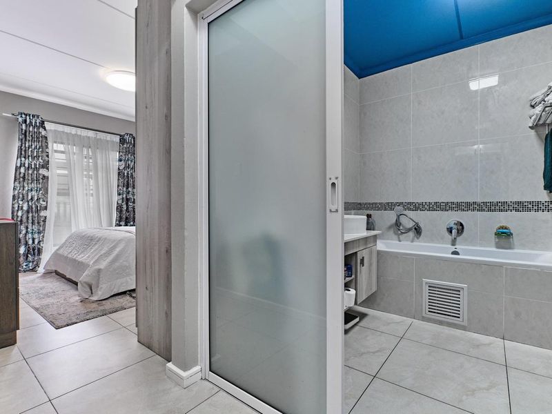 A modern bedroom featuring an en-suite bathroom with a built-in bathtub, vanity, and a sliding frosted glass door for privacy.